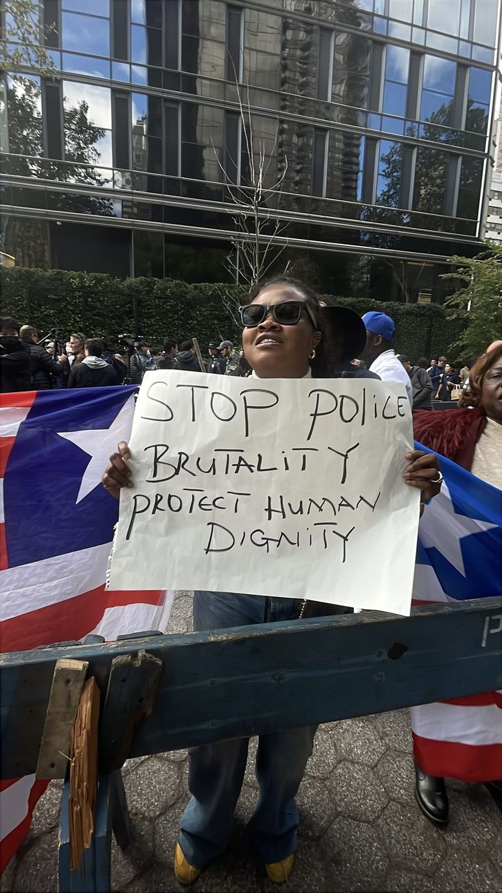Woman holding a sign reading Stop Police Brutality, Protect Human Dignity alongside a Liberian flag